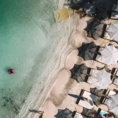 Widok z lotu ptaka na turkusowe morze i piaszczyste plaże Albanii. Jedna osoba relaksuje się na dmuchanym kole, a obok rzędy białych parasoli i leżaków.