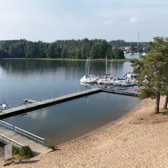 Słoneczna plaża nad jeziorem Wdzydze, z pomostami i żaglówkami. Idealne miejsce na wypoczynek.