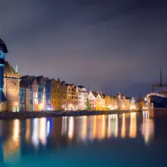 Nocny widok na Motławę w Gdańsku. Żuraw, zabytkowe kamienice i statek odbijają się w wodzie. Idealne miejsce na weekendowy wypad.