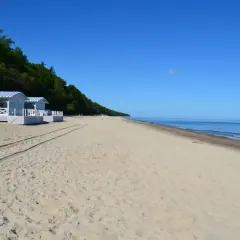 Pobierowo atrakcje: białe domki plażowe z niebieskimi markizami, piaszczysta plaża i spokojne morze pod błękitnym niebem.