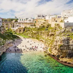 Malownicze klify i białe domy Polignano a Mare, z plażą pełną ludzi i turkusową wodą.