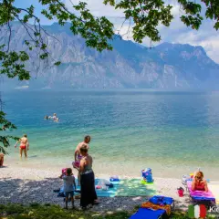 Ludzie odpoczywają na żwirowych plażach nad Jeziorem Garda, podziwiając góry.