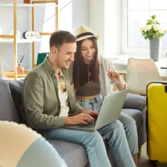 Para, planując kiedy majówka, przegląda oferty wakacyjne na laptopie. Obok walizki czekają na podróż.