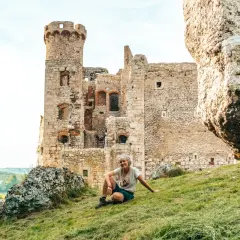 Kobieta odpoczywa na trawie przy ruinach zamku, idealne miejsce na przerwę podczas podróży szlakiem Orlich Gniazd samochodem.