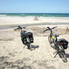 Dwa rowery z sakwami na piaszczystej plaży, gotowe na odkrywanie tras rowerowych nad morzem.