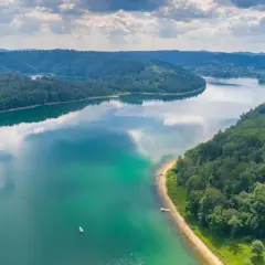 Malownicze jezioro otoczone lasami, idealne miejsce, gdzie warto pojechać nad jezioro w Polsce. Widać łodzie i piaszczystą plażę.