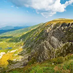 Widok na skaliste zbocze i zieloną dolinę z jeziorami. W oddali widać miasto. To krajobraz, który mógłby być nazwany "śnieżne kotły".
