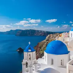 Santorini, idealne miejsce na wakacje w listopadzie gdzie najcieplej. Białe domy z niebieskimi kopułami nad lazurowym morzem.