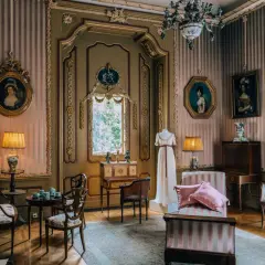 Eleganckie wnętrze pałacu w Nieborowie. W pokoju z różowo-białymi pasami na ścianach, stoją zabytkowe meble, obrazy i manekin z suknią.