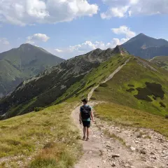 Mężczyzna z plecakiem idzie ścieżką przez zielone zbocza gór. Widok na grań i szczyty. Hala Ornak, trasa.