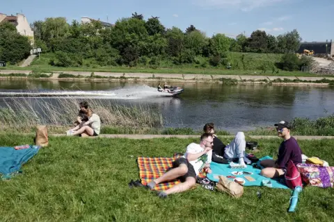 Majówka nad rzeką w Polsce: ludzie odpoczywają na trawie, a na wodzie ścigają się skutery wodne. Idealne miejsce, by spędzić wolny czas.
