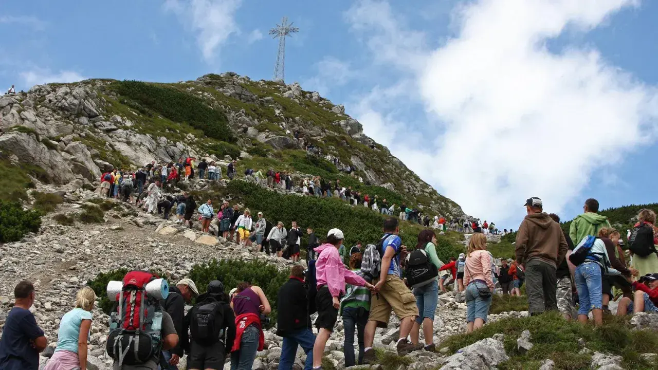 Tłum turystów na skalistej trasie na Giewont. W oddali widoczny krzyż.