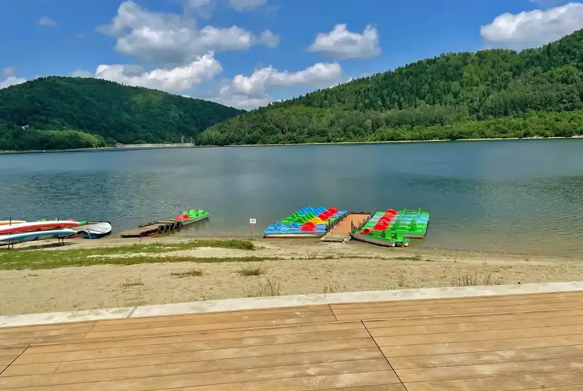 Kolorowe rowery wodne i kajaki czekają na plaży nad górskim jeziorem.