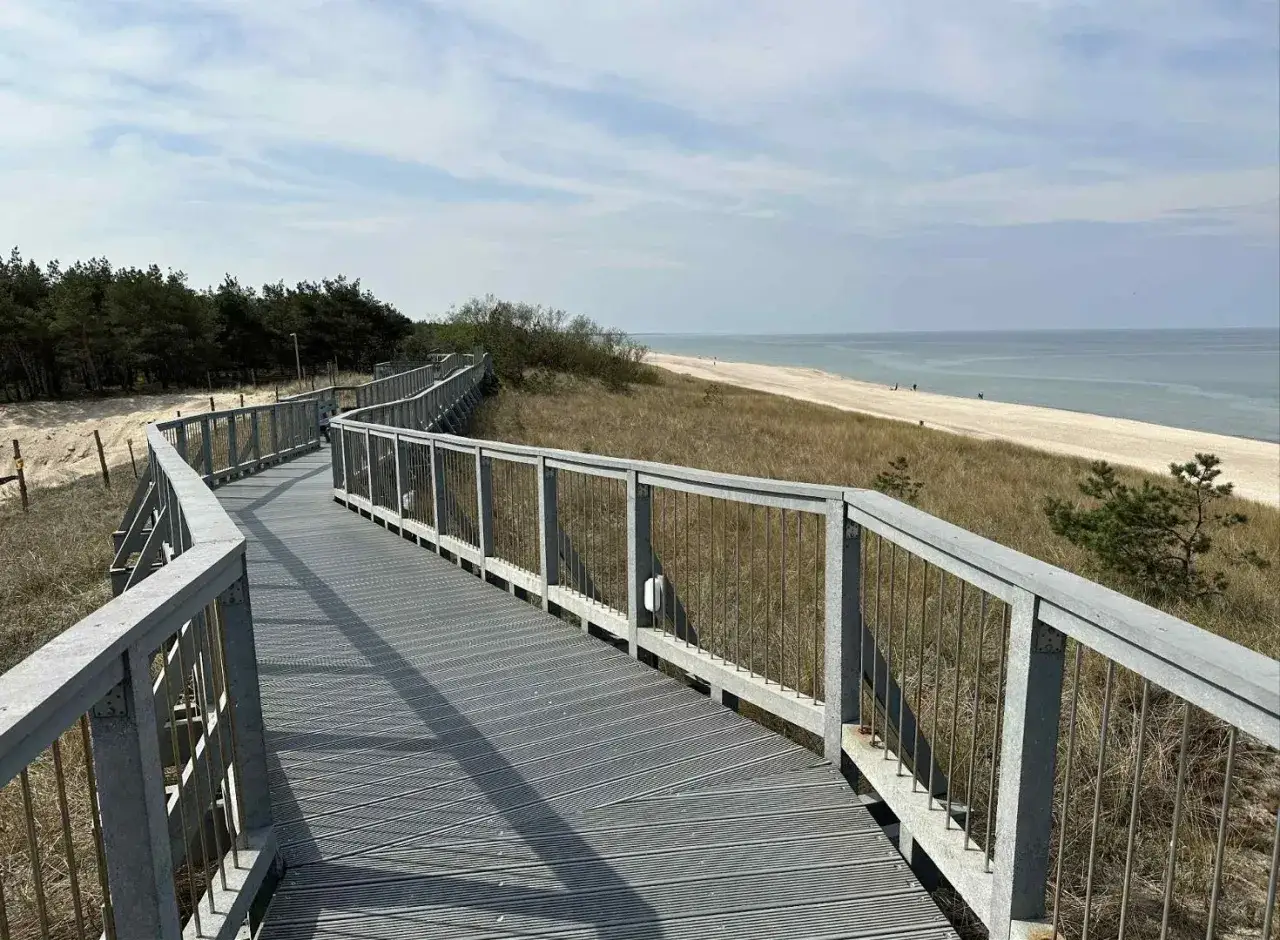 Długa, kręta promenada nad morzem prowadzi przez wydmy do piaszczystej plaży.