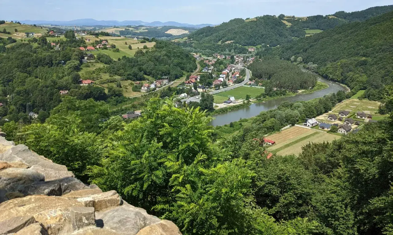 Widok na dolinę Popradu z Rytrem, gdzie widać zabudowania, rzekę i wzgórza. Zamek Rytro góruje nad krajobrazem.