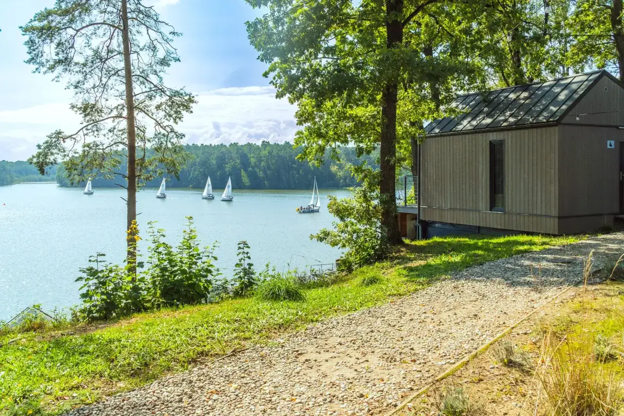 Żaglówki na jeziorze w Rucianem Nidzie. Nowoczesny domek nad wodą, otoczony zielenią.